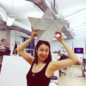 a photo of Mari Miller holding tiles made from paper pulp over her head like an oversized crown